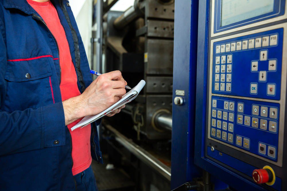 Tecnico annota dati su un controller industriale accanto a una pressa a iniezione